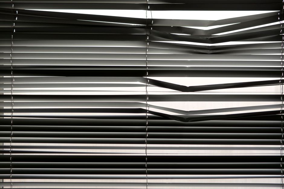 Horizontal venetian blinds creating a shadow pattern indoors with strong sunlight.