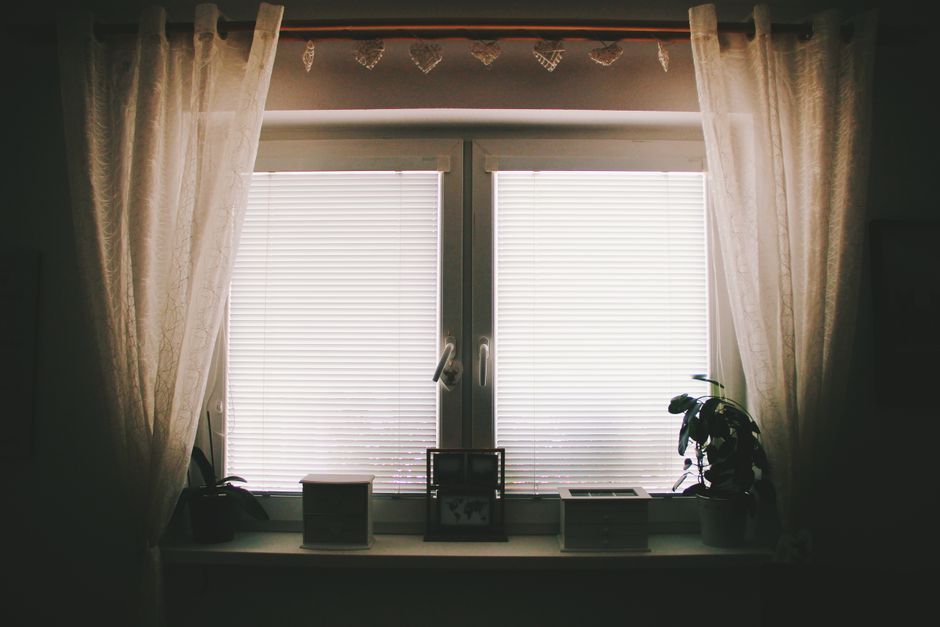 A home interior featuring a window with curtains, blinds, and potted plants.
