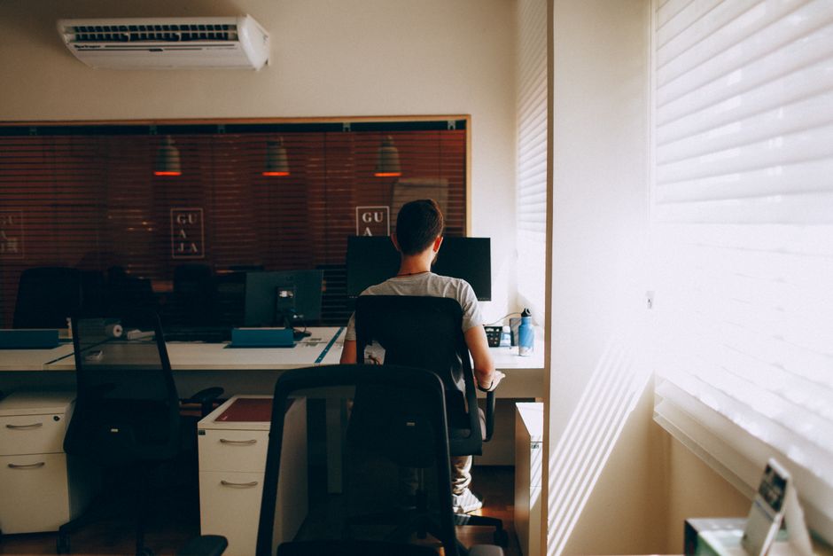 Man working at desk in modern office with computer, sunlight through blinds.