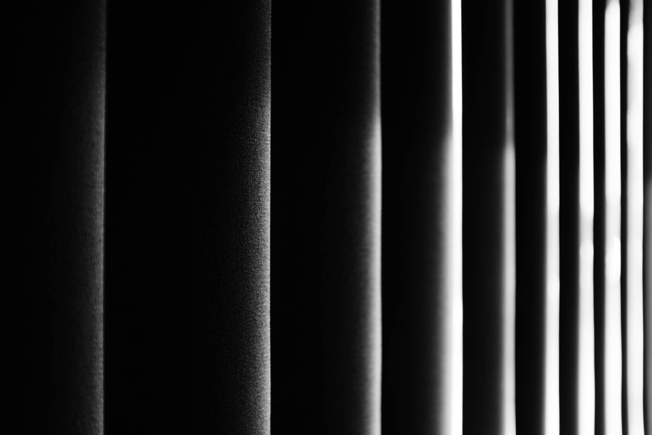 Moody black and white photo emphasizing vertical blinds with soft light and shadows.