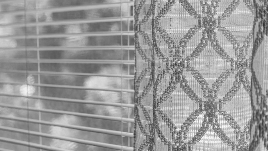 Close-up texture of a decorative curtain and blinds in grayscale.